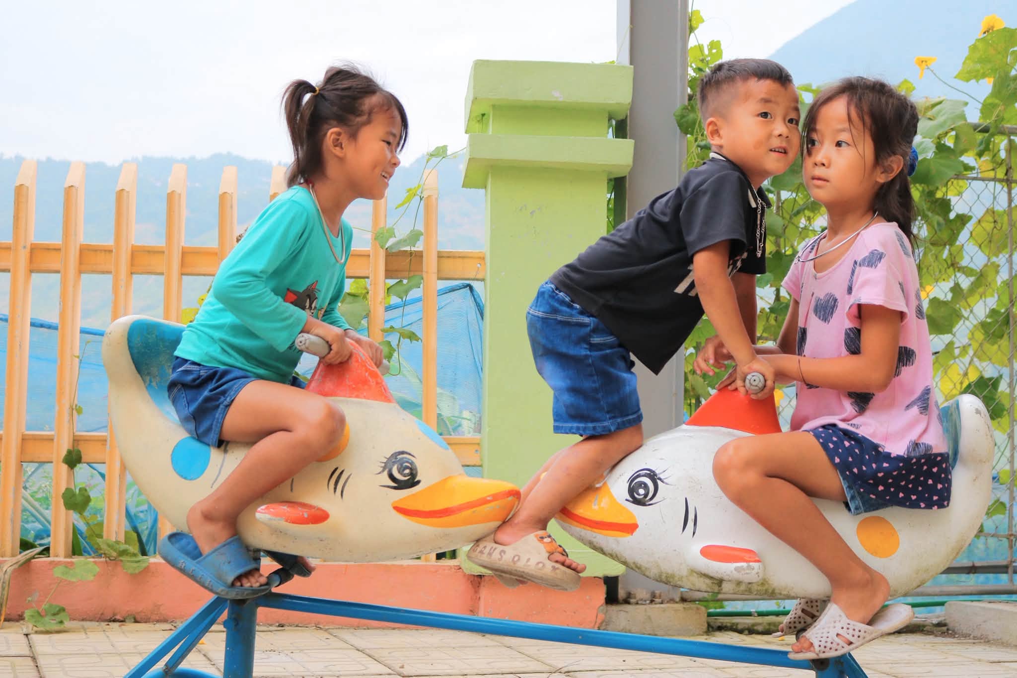 Ba em nhỏ chơi bập bênh hình chú vịt trong sân trường