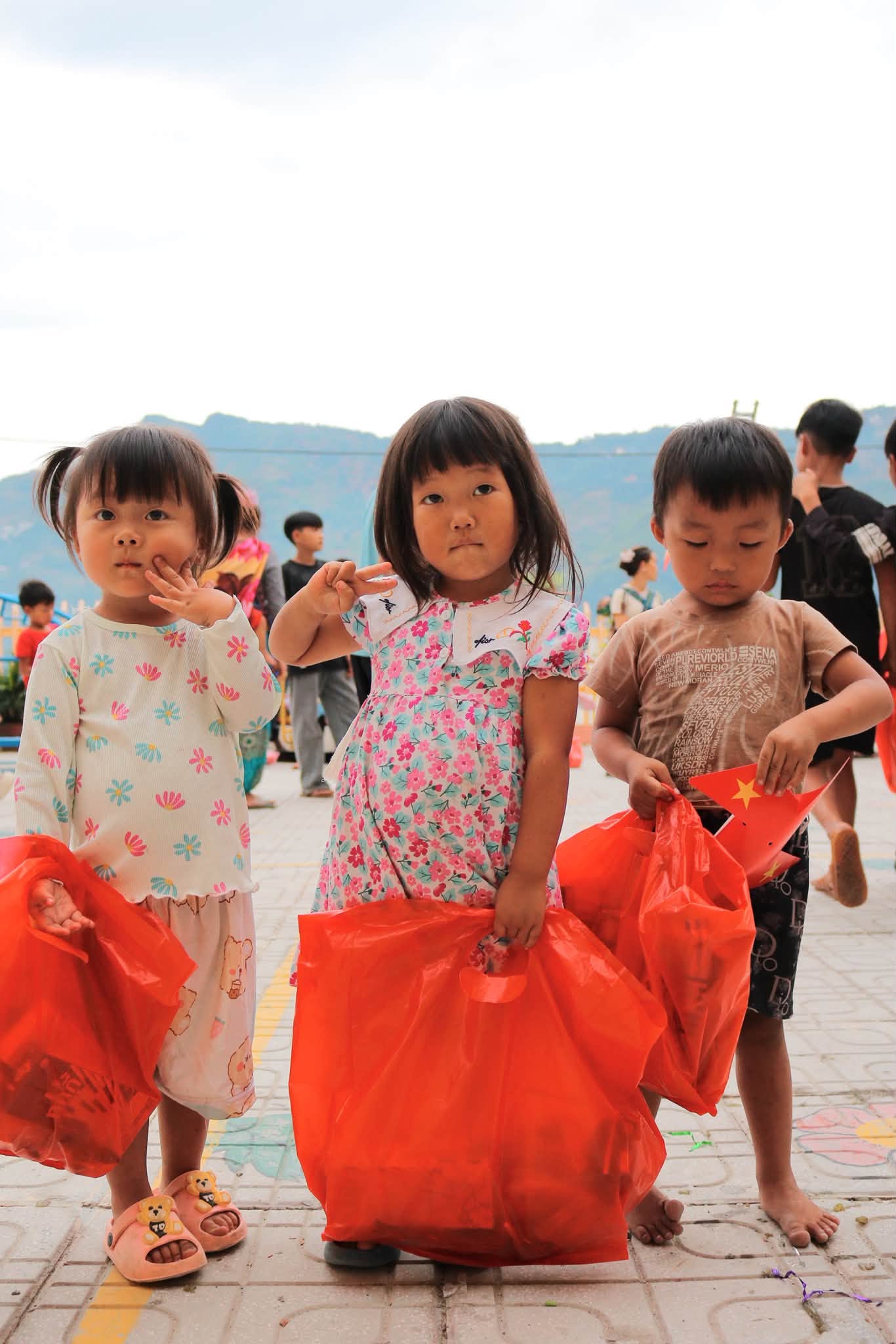 Các em nhỏ ôm túi quà đỏ giữa sân trường