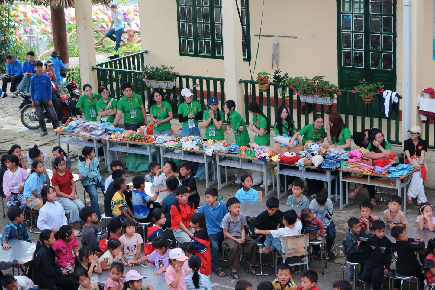 Các em nhỏ ngồi theo bàn dài nhận quà tại sân trường